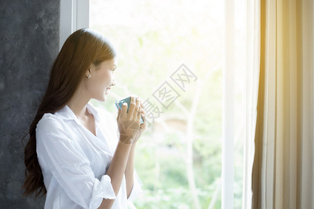 早晨漂亮的吸引人亚裔妇女喝咖啡在床上醒来后完全休息清晨打开窗帘以获得阳光的新鲜空气亚洲妇女喝咖啡在床上醒来图片