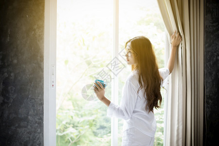 美丽的亚裔妇女喝咖啡在床上醒来后完全休息清晨打开窗帘以获得阳光的新鲜空气亚洲妇女喝咖啡在床上醒来马克杯热的图片