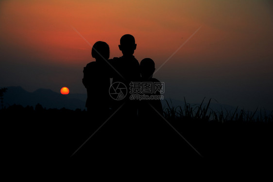 亚洲男生三个孩子的黑色轮盘一起站在日落时有天空商业图片