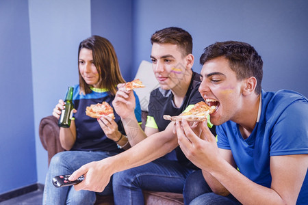 足球迷在沙发上看球吃披萨图片