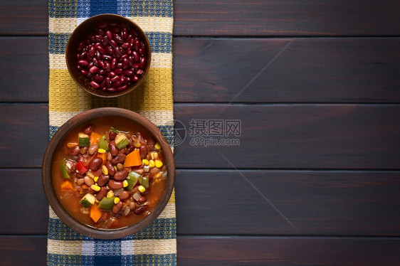 一顿饭用肾豆胡萝卜青尼白胡椒甜玉米番茄洋葱大蒜上面碗中的生豆子在黑木上用天然光拍照骗局多于图片