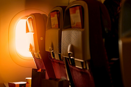 空气游客座位经济舱椅的后视图纸质小册子插在塑料飞机托盘桌上的盒子里阳光穿过经济舱飞机窗户进入乘旅行的概念图片