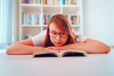 架子货松弛在书前躺的地板上身戴眼镜持有一本书的年轻美女学生在家里阅读或学习的肖像图片