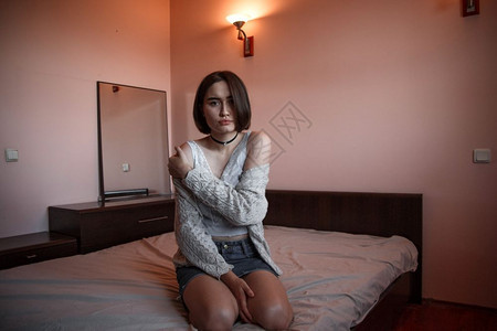压力情感沮丧的一个穿着毛衣短发和牛仔裙的年轻女孩独自坐在卧房的床上压抑中独居图片