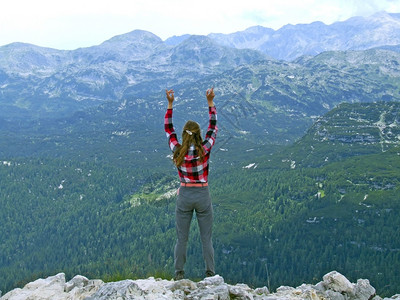 年轻女站在悬崖角边缘用举起的手仰望天空年轻旅游者在山顶上旅游中欢欣快乐女孩安息在山上活跃的生方式年轻女站在悬崖角边以举起的手图片