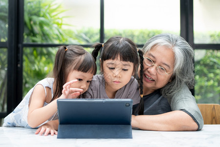 初级亚洲祖母与两个孙子女一起在客厅用数码平板电脑在家玩教育游戏享受乐趣和在线教育游戏网上和父母照顾的概念学生家长的关心习活图片