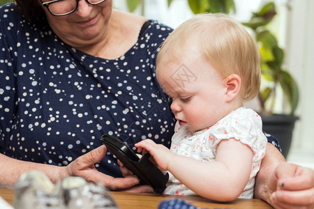 母亲女士快乐的祖母和可爱孙女使用智能手机教客厅快乐的祖母和可爱孙女使用智能手机教学愉快图片