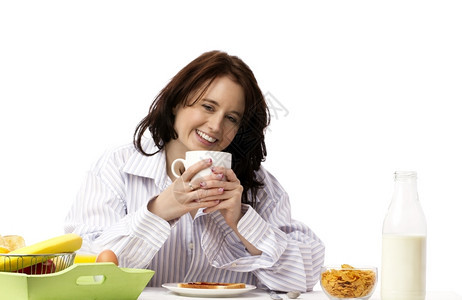 享受女士年轻笑人在早餐时拿着咖啡杯的年轻笑女人在早餐时明亮的图片