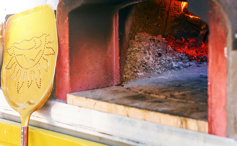 优质的热红色用木柴烤火炉用骨灰比萨烧香剂和火烤炉的子有一把黄色铲子旦准备好就从烤箱中拿起披萨图片