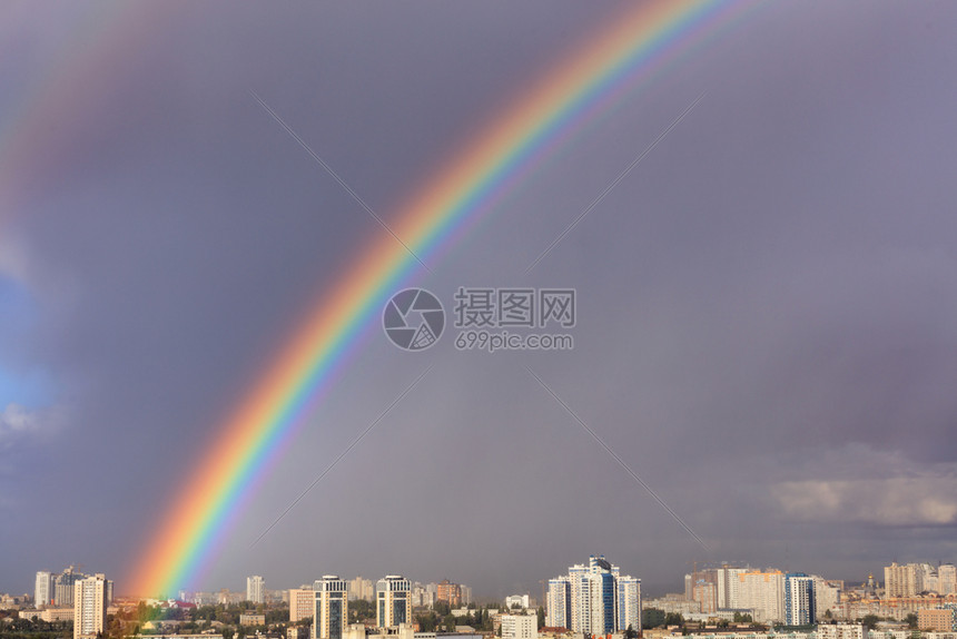 超过视窗在最后一场雷暴之在城市房屋上方灰云的天空中一个闪亮而稠密的大彩虹最后一次雷暴之在城市上空的灰色天中有一个巨大的明彩虹颜色图片