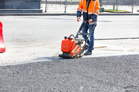 夯公路工人用汽油振动式压机铺有汽油振动式压机的沥青在道路修理工点使用电动板压缩沥青路面人行道图片