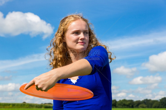 投掷运动夏天年轻caucasian年轻女人拿着橙色飞盘户外对着蓝天图片
