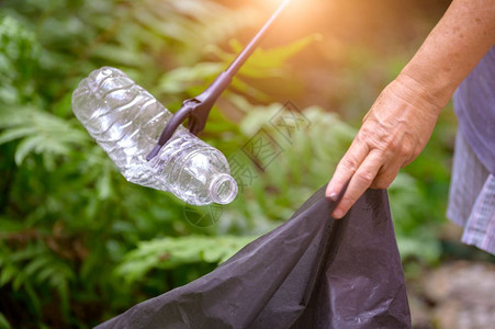 户外人们技巧将饮用塑料瓶的废物收集成袋装生态和环境关注事项的手持和废物抓捕者紧关地把饮用水塑料瓶废物收集起来回废物处理技术图片