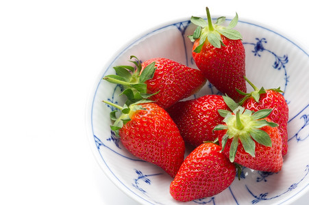 蓝色的有机新鲜成熟草莓抗氧化剂和维生素C的来源放在一个有蓝色装饰模式的白碗中作为健康的零食或甜点在白色上提供复制空间的高角缝合服图片