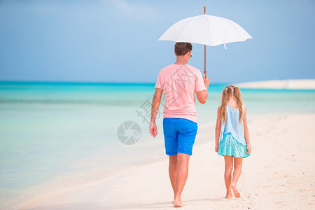父亲和女儿在海滩上带着雨伞躲避阳光图片