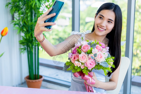 花束情人节概念快乐的自喜笑的亚裔年轻女坐在餐桌食物里厅背景中盛着一束玫瑰花植物群幸福图片