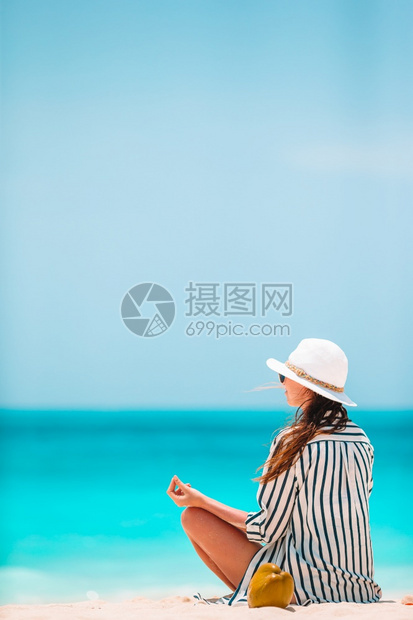 游客在白色沙热带海滩上做瑜伽的年轻美女在海滩上穿绿礼服的年轻时尚女郎太阳图片