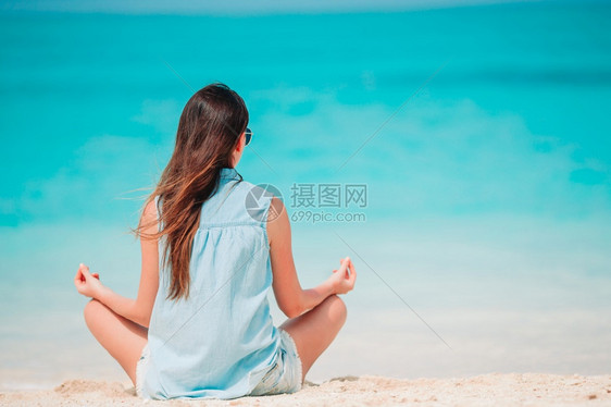 在白色沙热带海滩上做瑜伽的年轻美女在海滩上穿绿礼服的年轻时尚女郎保持乐趣士图片