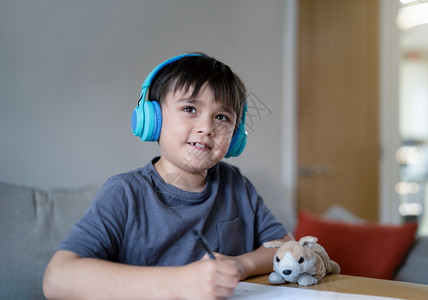 童年娱乐随意的快孩子戴耳机在画纸时聆听音乐室内肖像可爱的年轻男孩微笑地仰望着脸积极的儿童周末在家享受创造活动图片