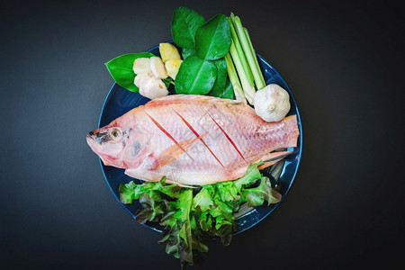 亚洲人最佳叶子在为烹饪准备的黑桌陶瓷盘中新鲜鱼和蔬菜的最顶端视图图片