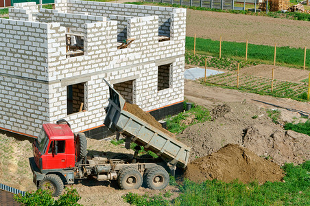 建设者挖土机掘地面土机作为桶子工在挖土机用桶子正在建造的房屋未完工白砖屋私人房中进行挖土机运货作品图片