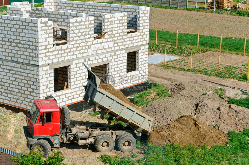 建设者挖土机掘地面土机作为桶子工在挖土机用桶子正在建造的房屋未完工白砖屋私人房中进行挖土机运货作品图片