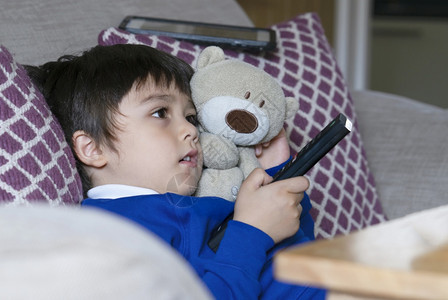 幸福学前班幼童坐着泰迪熊看电视快乐的孩子拥抱棕熊玩具握着遥控器小男孩放学后在家松一下YA年轻的图片