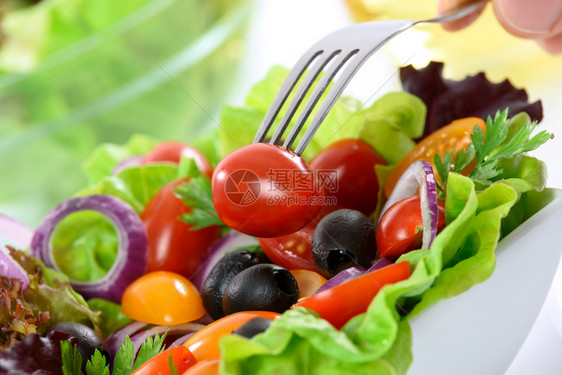 健康营养的概念餐桌上碗中混合蔬菜沙拉和手拿着番茄叉子的一只手卫生保健小吃可口图片