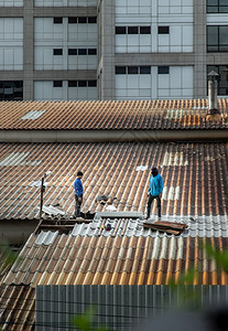 爬承包商装修泰国曼谷201年5月8日两名打杂工人在被损坏的工厂屋顶上修理瓷砖图片