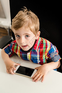小男孩坐在办公椅子上时抬头玩智能手机显示他的舌头反映了注意力电话屏幕是空白的很容易被你所想要的应用程序屏幕所取代现工具通讯简洁易图片