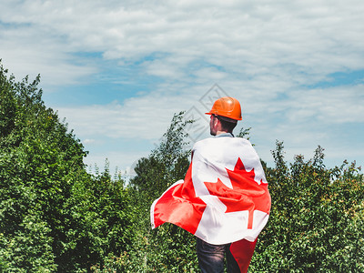 头盔天有吸引力的工程师在绿树和落日背景下在公园中悬挂加拿大研究距离近的劳动和就业概念青年工程师橙色硬帽和加拿大在绿树和日落的背景图片