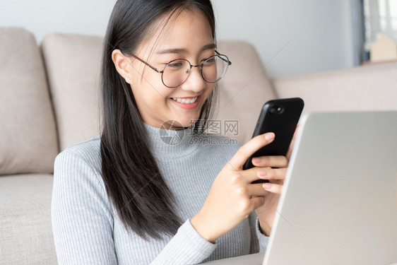 保持乐趣坐着美丽的亚洲年轻女使用智能手机与朋友的亚洲女孩聊天在家中客厅用智能电话进行视频通校对Portnoy图片