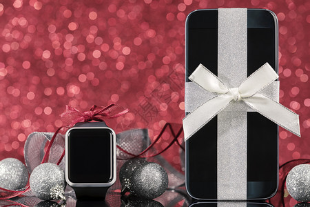经典的软垫红背景黑玻璃桌上圣诞树智能手机和表及装饰红色背景的黑玻璃桌子上圣诞树屏幕图片