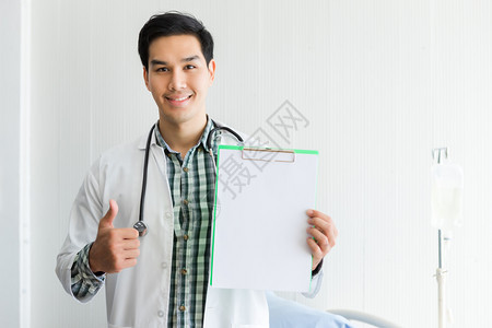 英俊的亚洲年轻男子医生治疗咨询与积极情绪保持空剪贴板显示拇指举起和床位在医院背景复本空间的病情中男文档图片