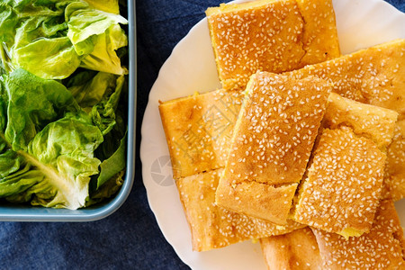 吃桌子树叶玉米面包松饼的顶端景色在蓝碗桌边面上用芝麻种子覆盖的白盘中新鲜绿色沙拉有机素食品图片