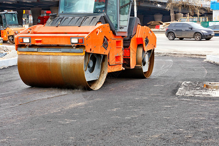 重的压实机更新型橙色振动溜冰场在新建道路城市街的施工中压实热沥青带有复制空间的图像重型道路振动压机在新的道上压实鲜沥青图片