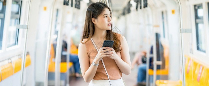 泰国离开使用智能手机的亚洲年轻女乘客在大城市通勤和交中旅行时寻找地铁列车外的坐客概念在大型城市上下班者和运输方面上市图片