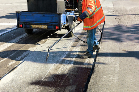 维护道路修工人将沥青混合物喷洒到清洁地区以更好粘合新的沥青对路进行部分修理工人在沥青表面喷洒在表面喷洒机械雾剂图片