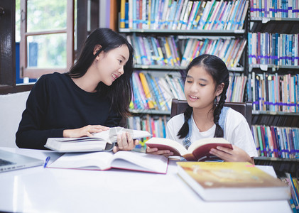 坐着书架前的两个女学生一起阅读书籍图片