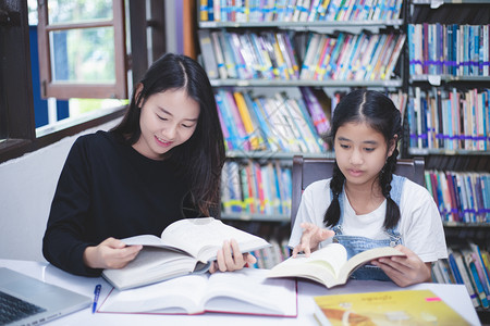 坐着书架前的两个女学生一起认真看书图片