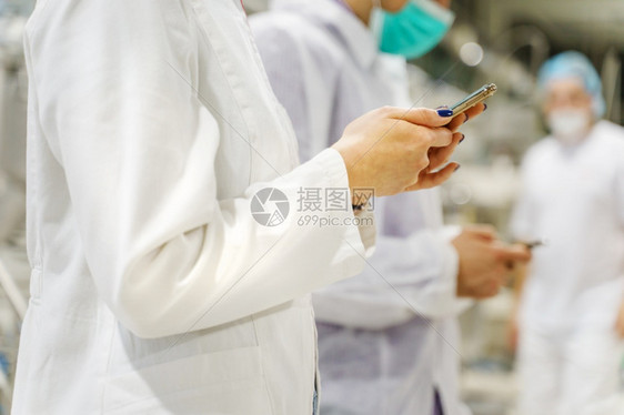 关于在医院拥有智能手机的不明天主教女医生在手术室医院使用移动电话的外科医生疗工作者小组技术医学概念的近距离中场手术室内使用移动电图片