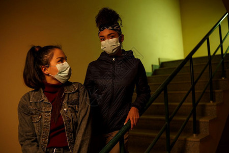 流感异族新冠在楼梯井有选择地重点救助避免感染的一次医疗保护面罩上身着一次医疗保护面罩的亚裔和非洲年轻女孩跨种族国际援助友谊图片