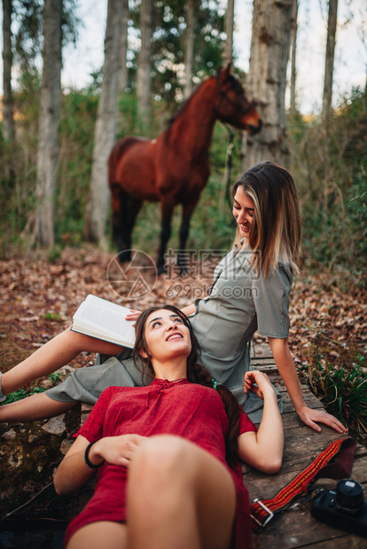 金发女郎连衣裙年轻一对身着洋装的年轻女子正在阅读一本书森林里用旧相机和马拍照旅行图片