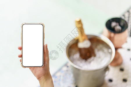 蜜月妇女手握空白屏幕移动电话在冰桶里装香槟瓶在按摩池附近有两杯玻璃水池靠近图片