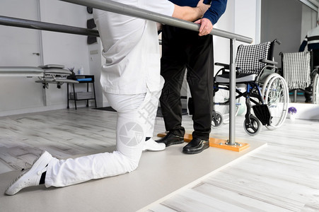 物理治疗师帮助残疾白种人老在康复中心用双杠走路高品质照片物理治疗师帮助残疾白种人老在康复中心用双杠走路医生男残疾人图片
