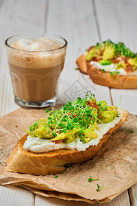 素食主义者加奶油乳酪微绿和芝麻种子的鳄梨三明治贴近加卡布奇诺的纸衬玻璃上有选择地聚焦于蔬菜烤面包的早餐概念法国面包复制图片