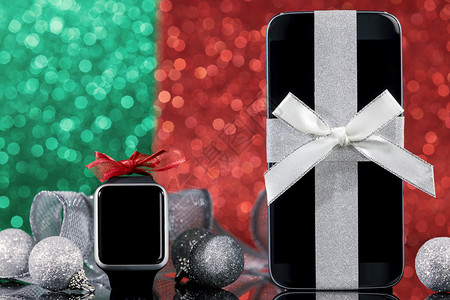 绿色和红背景的黑玻璃桌对面圣诞树上智能手机观察和装饰及关注智能手机散景灯经典的图片
