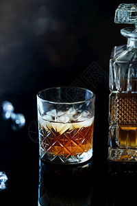 黑色的一杯威士忌或波旁在黑石桌上加冰一杯的威士忌和一个方形醒酒器一杯苏格兰威士忌和冰优质的结石图片