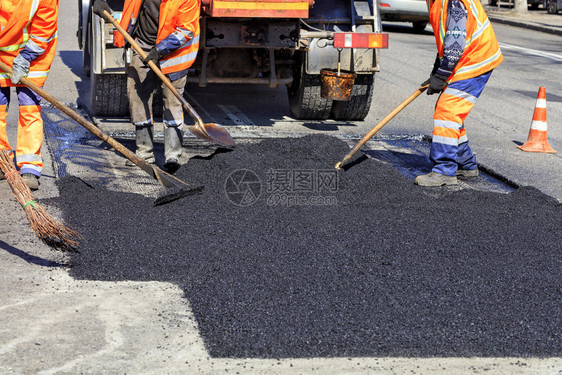 碎石乌克兰热的道路工人作组以新鲜热沥青来更部分公路并平滑其修补工作组在修复公路时手工用铲子擦干热沥青用铲子粉刷热沥青图片