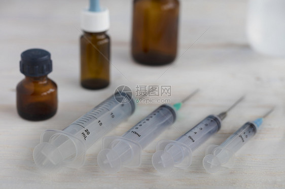 各种能力的医疗注射器和用瓶子在白木板上的色彩漆木制桌面上对方白木制桌面上有环状物和医疗护囊治虐待类固醇图片